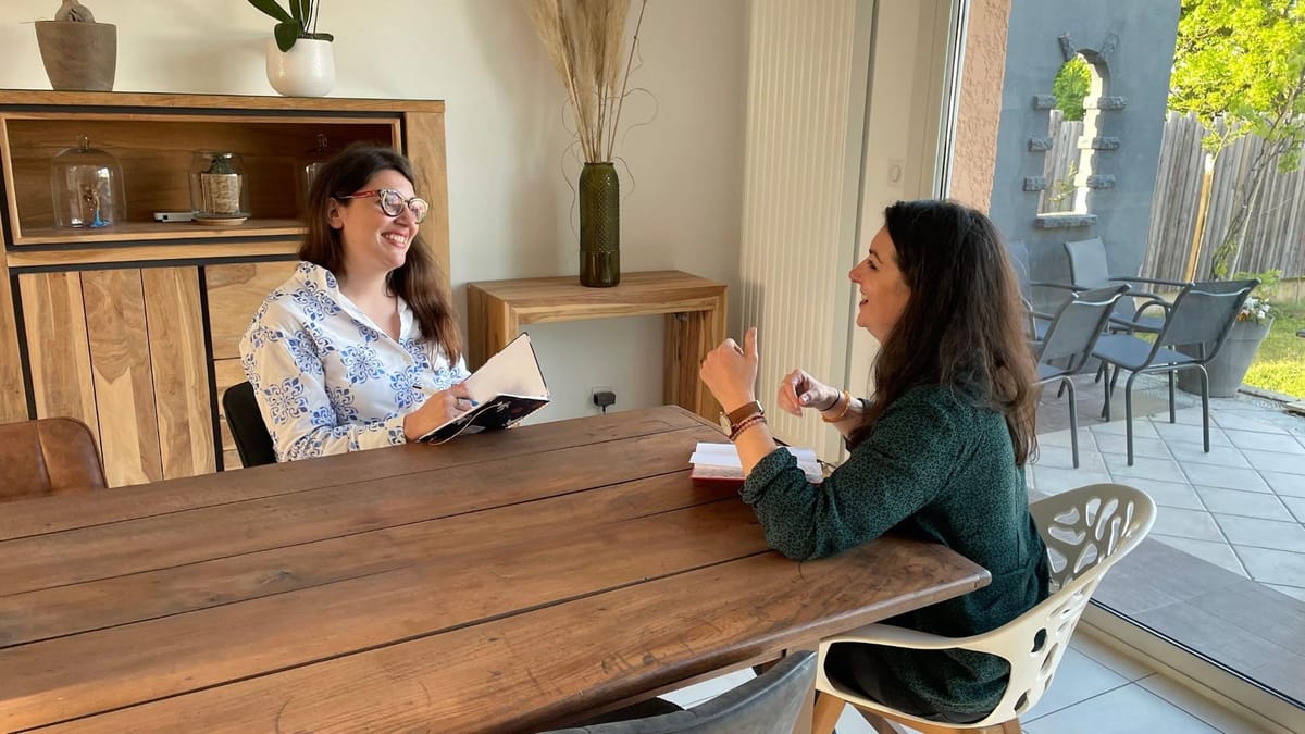 Aurélie Picard en rendez-vous de bilan de compétences, carnet en main, échangeant en souriant avec une personne assise de l’autre côté d’une table en bois